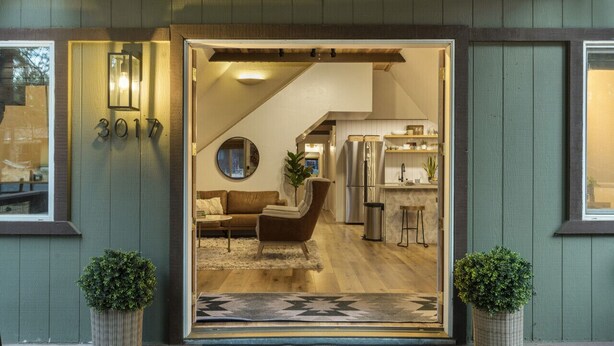 A modern interior with a sofa, chair, and kitchen area visible through an open door. - A-frame cabin, fenced-in yard (Flagstaff)