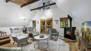 A loft-style living room with a fireplace, seating, and a large window. - A-frame cabin, fenced-in yard (Flagstaff)