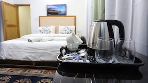 Quarto de hotel com cama, bandeja com copos e chaleira, e um quadro na parede.