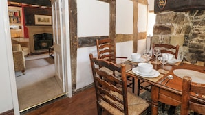 A traditional dining room with a wooden table set for four, surrounded by wooden chairs. A stone wall and a fireplace are visible in the background. - Pentre Hall (Oswestry)