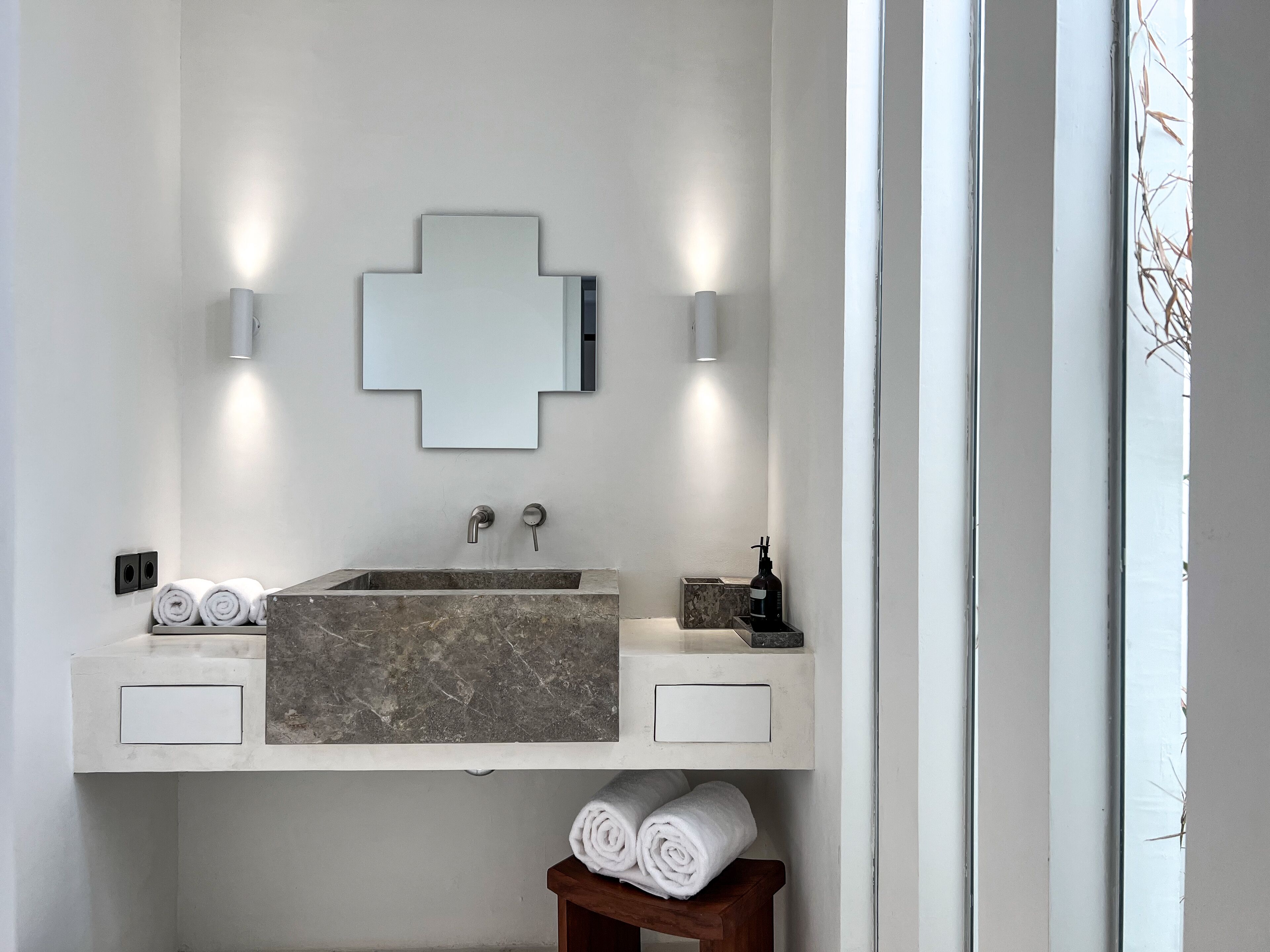 A modern bathroom with a large mirror, two wall-mounted lights, a marble sink, and two towel racks.
