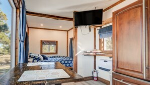 Un intérieur de camping-car compact comprenant un lit, une table avec des documents, un téléviseur fixé au mur et une petite kitchenette.