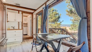 L’intérieur chaleureux d’un chalet comprend une table à manger, des meubles en bois et une grande fenêtre donnant sur un paysage de forêts et de montagnes.