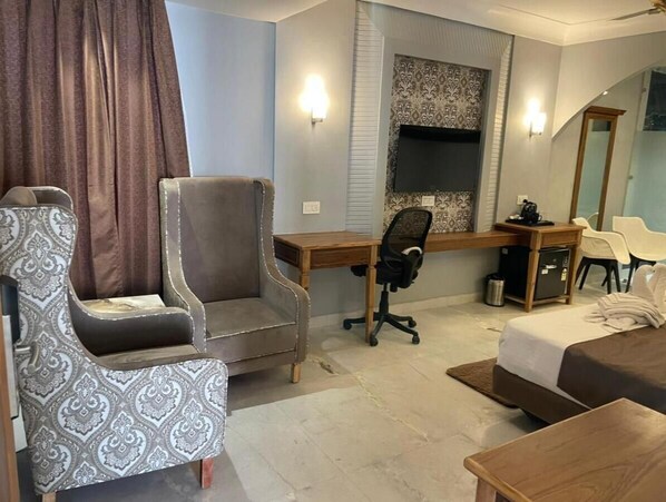 A modern hotel room with a large bed, a desk with a computer, a comfortable armchair, and a large mirror.