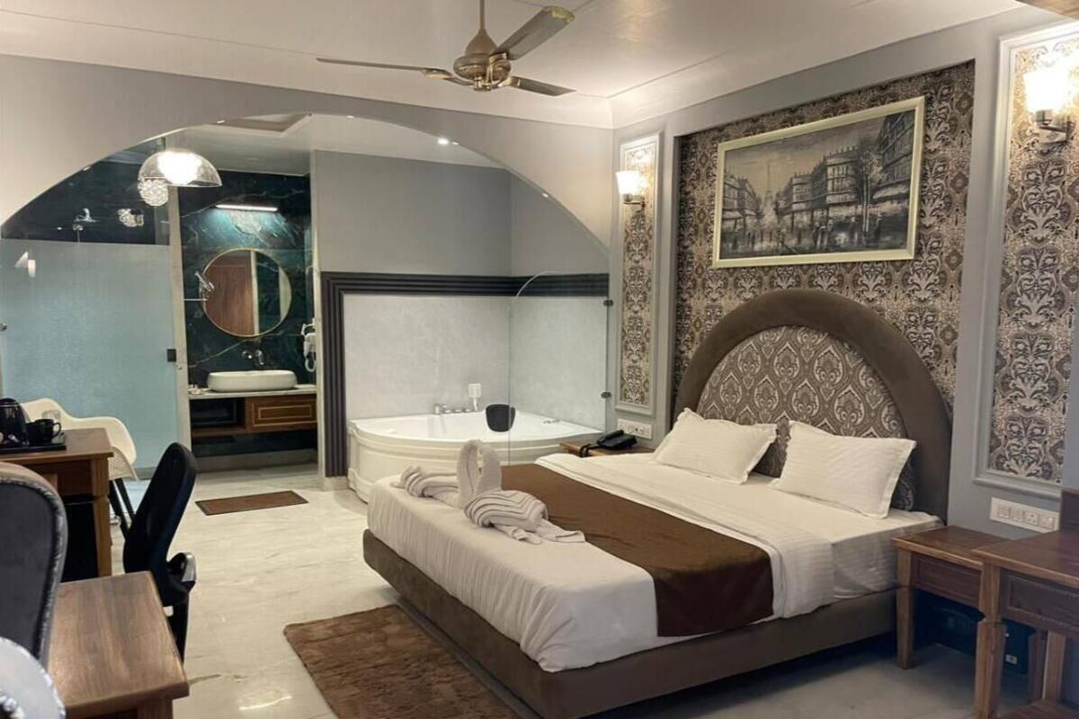 Een moderne hotelkamer met een groot bed, een zithoek met bureau en stoel, een aparte badkamer met badkuip, en een plafondventilator.