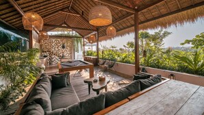 Un espacio exterior tipo salón con mesa de billar, asientos cómodos y vistas a exuberante follaje.