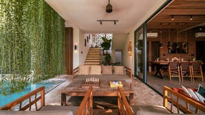 Un salón amplio con una mesa de centro de madera, asientos acolchados, un tablero de ajedrez y vistas a una escalera que conduce a una zona de cocina.
