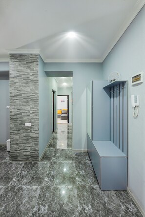 A hallway with a stone wall, a marble floor, and a reception area with a phone and a coat rack. - H&B apartments Queen Ketevan (Tbilisi)