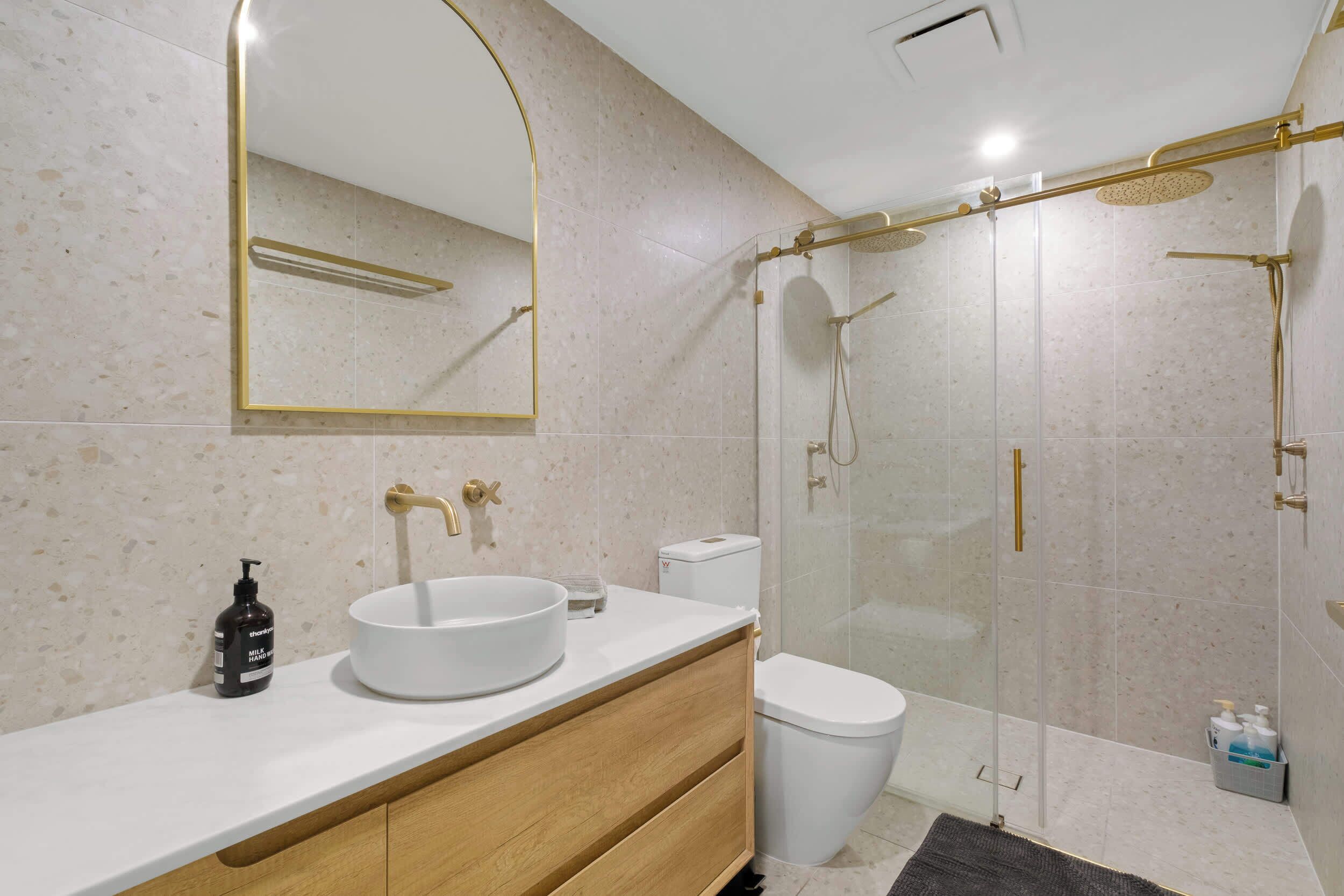 A modern bathroom with a white sink, a large mirror, a glass-enclosed shower, and a toilet.