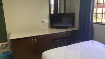 A hotel room with a bed, a TV on a dresser, a window with curtains, and a trash bin.