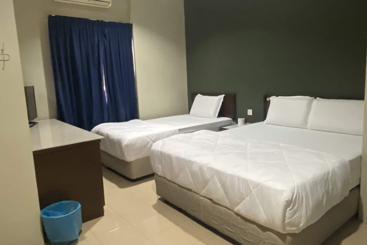Une chambre d’hôtel avec deux lits simples, un bureau, une chaise, une poubelle bleue et un appareil de climatisation.