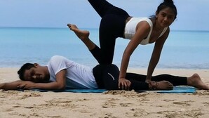 Two individuals practicing yoga on a beach with the ocean in the background. - BM Loft On Nut & Massage (Bangkok)