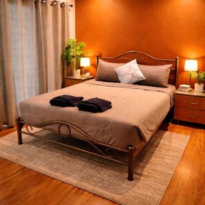 A neatly made bed with a metal frame, two pillows, and a blanket. There are two bedside tables with lamps and a potted plant. - BM Loft On Nut & Massage (Bangkok)