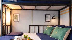 A bunk bed room with a blue and white color scheme, a bedside table with a lamp, and a tray with towels and fruits. - BM Loft On Nut & Massage (Bangkok)
