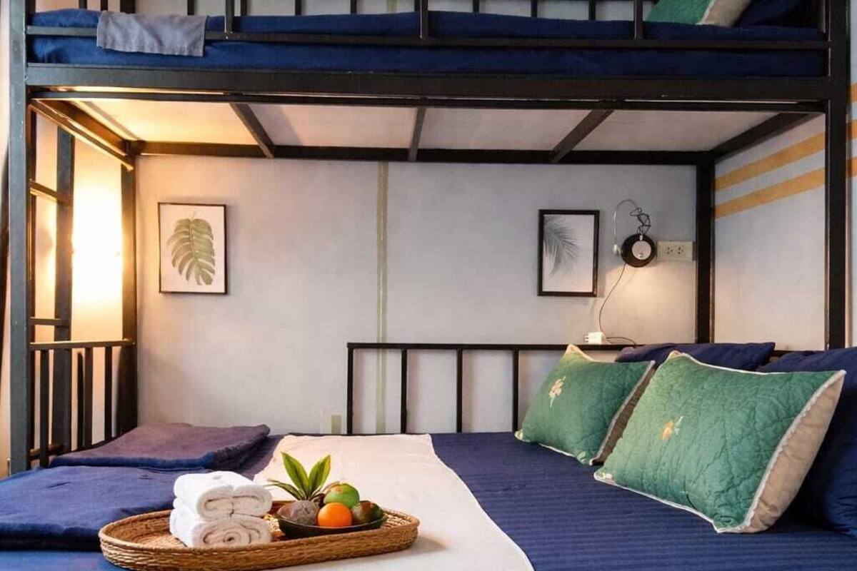 A bunk bed room with a blue and white color scheme, a bedside table with a lamp, and a tray with towels and fruits.