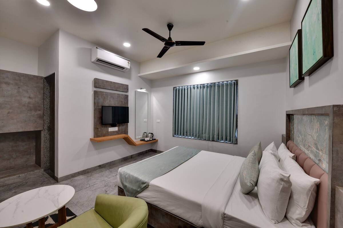 Une chambre d’hôtel moderne équipée d’un lit, d’un fauteuil vert, d’une petite table, d’un ventilateur de plafond et d’un téléviseur.