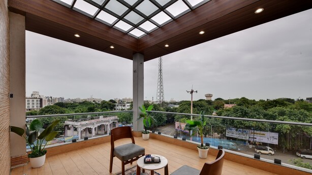 Un balcón con dos sillas y una mesa pequeña, con vista a un paisaje urbano de edificios y áreas verdes.