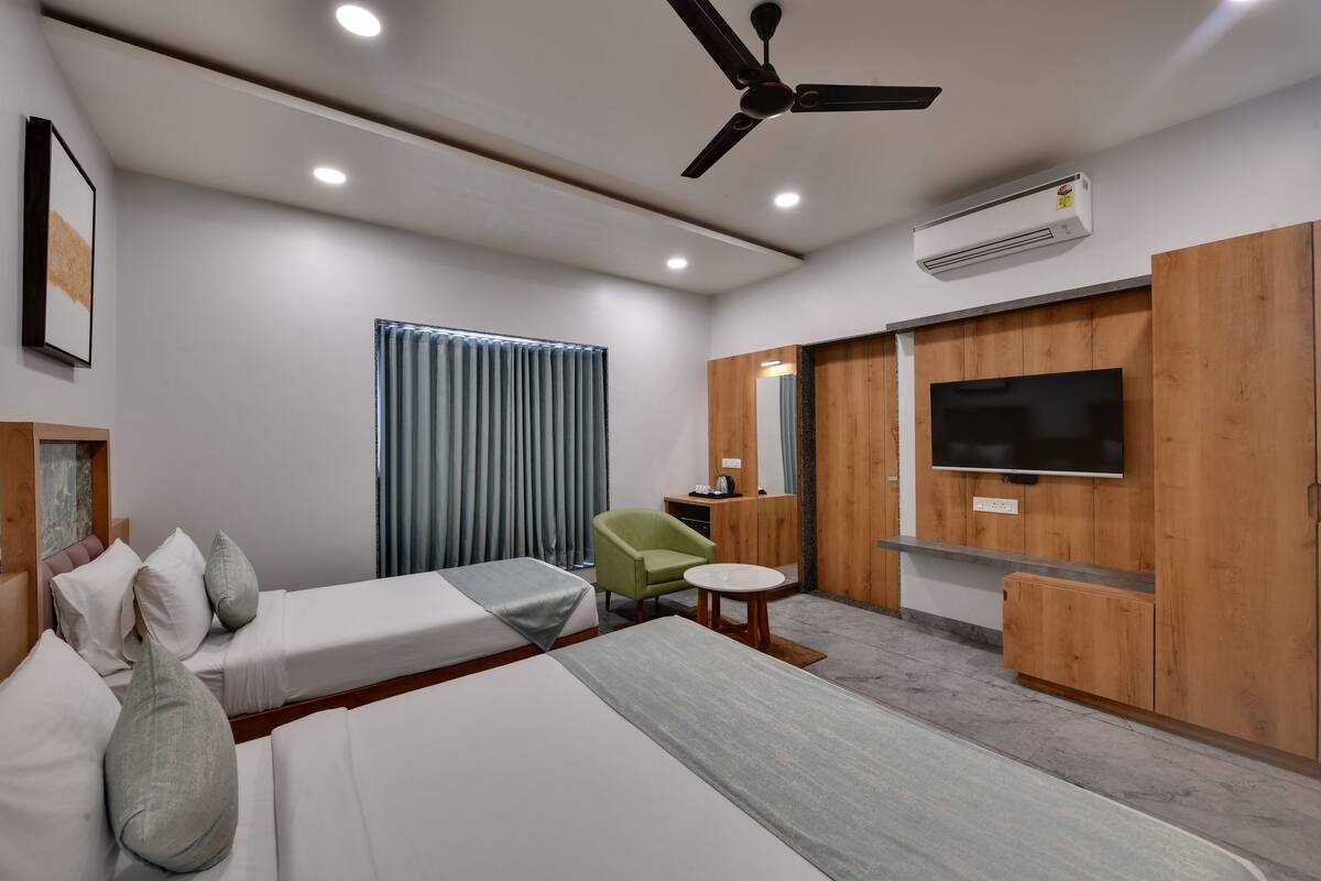 Une chambre d’hôtel avec deux lits, un fauteuil vert, une petite table ronde, un téléviseur et un ventilateur de plafond.