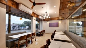Un comedor moderno con vigas de madera en el techo, mesas de mármol y asientos acolchados.