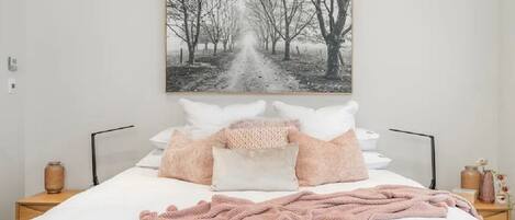A neatly arranged bedroom with a large bed, a framed picture above it, and bedside tables with lamps.