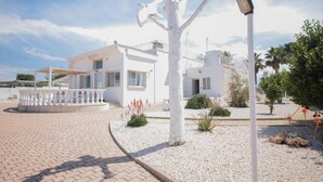 A modern white building with a circular driveway, a white tree sculpture, and a street lamp.