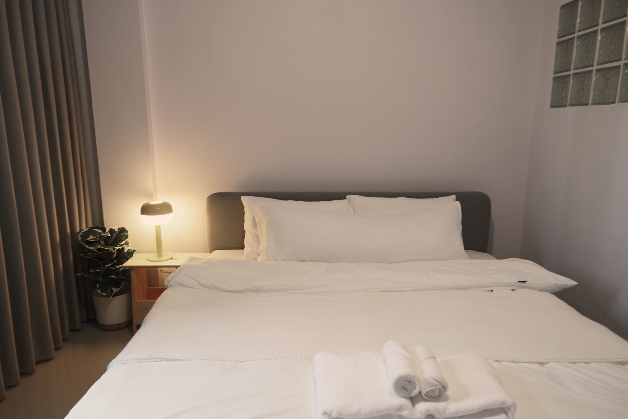 A neatly made bed with white linens, a bedside lamp, and a potted plant.