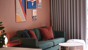 A modern living room with a green sofa, red and blue cushions, a small round table, and abstract wall art. - 4 Bedrooms, Private&Cozy @ Walking Street (Chang Wat Chiang Rai)