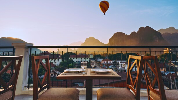 A table set with plates and glasses on a balcony overlooking a mountainous landscape. - Oudomsin VangVieng Hotel (Vang Vieng)