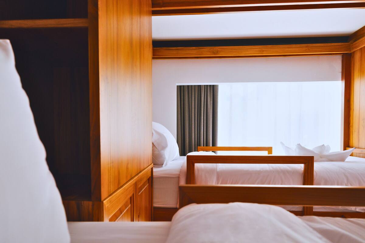 Een hotelkamer met twee houten bedden, een kledingkast en een groot raam met gordijnen.