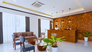 A modern reception area with a wooden reception desk, seating arrangements, and large windows. - Oudomsin VangVieng Hotel (Vang Vieng)