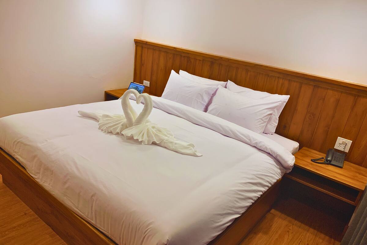 Een hotelkamer met een net opgemaakt bed, een houten hoofdbord, een nachtkastje met telefoon en een stopcontact.