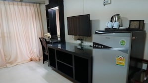 Una habitación pequeña con escritorio, televisor y refrigerador.