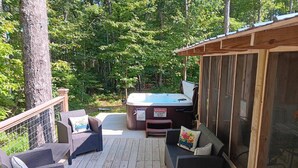Une terrasse dotée de meubles en osier et d’un jacuzzi, le tout entouré d’arbres.