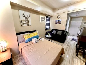 A hotel room with a bed, a sofa, a small table with a plant, and a wall clock.
