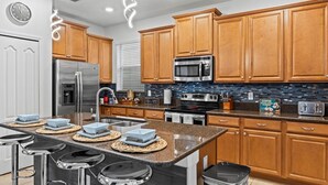 Une cuisine moderne avec des meubles en bois, des appareils en acier inoxydable, un îlot central doté de tabourets et un pare-feu orné de carreaux bleus.