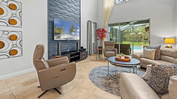 Un salon spacieux au design moderne, doté d’un grand téléviseur à écran plat, de sièges confortables et offrant une vue sur une piscine.