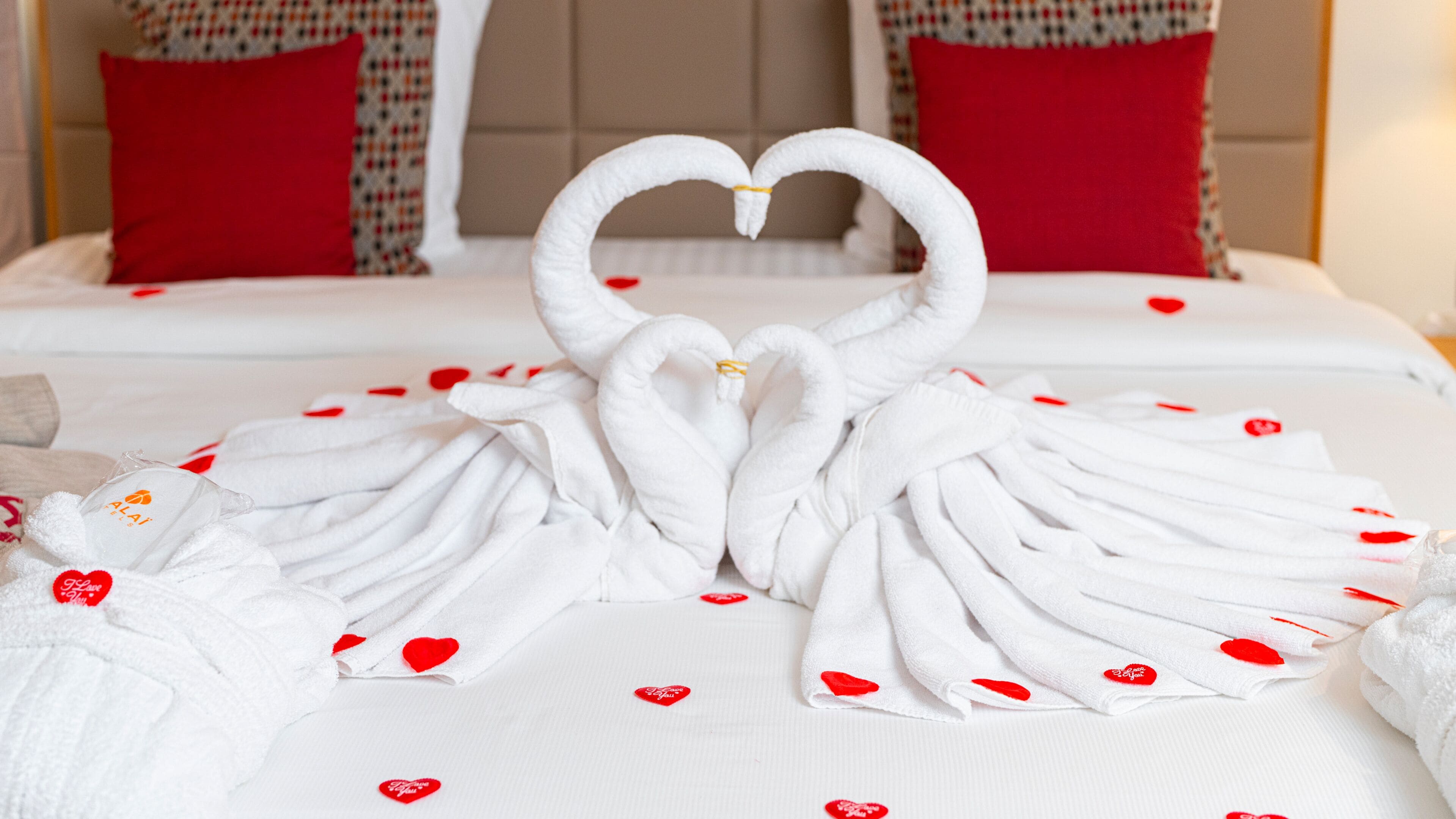 A bed with white linens and red heart-shaped pillows.