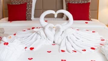 A bed with white linens and red heart-shaped pillows.