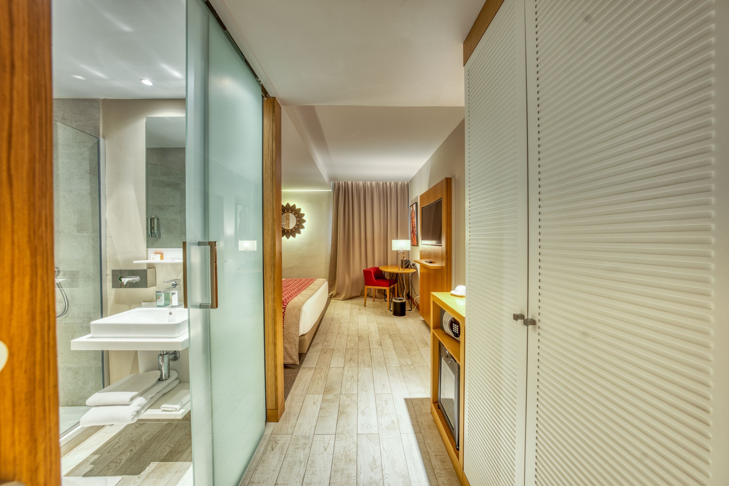 A hotel room with a shower, sink, bed, bedside table, and a wardrobe.