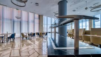 A modern dining area with a long table, chairs, and a central column.