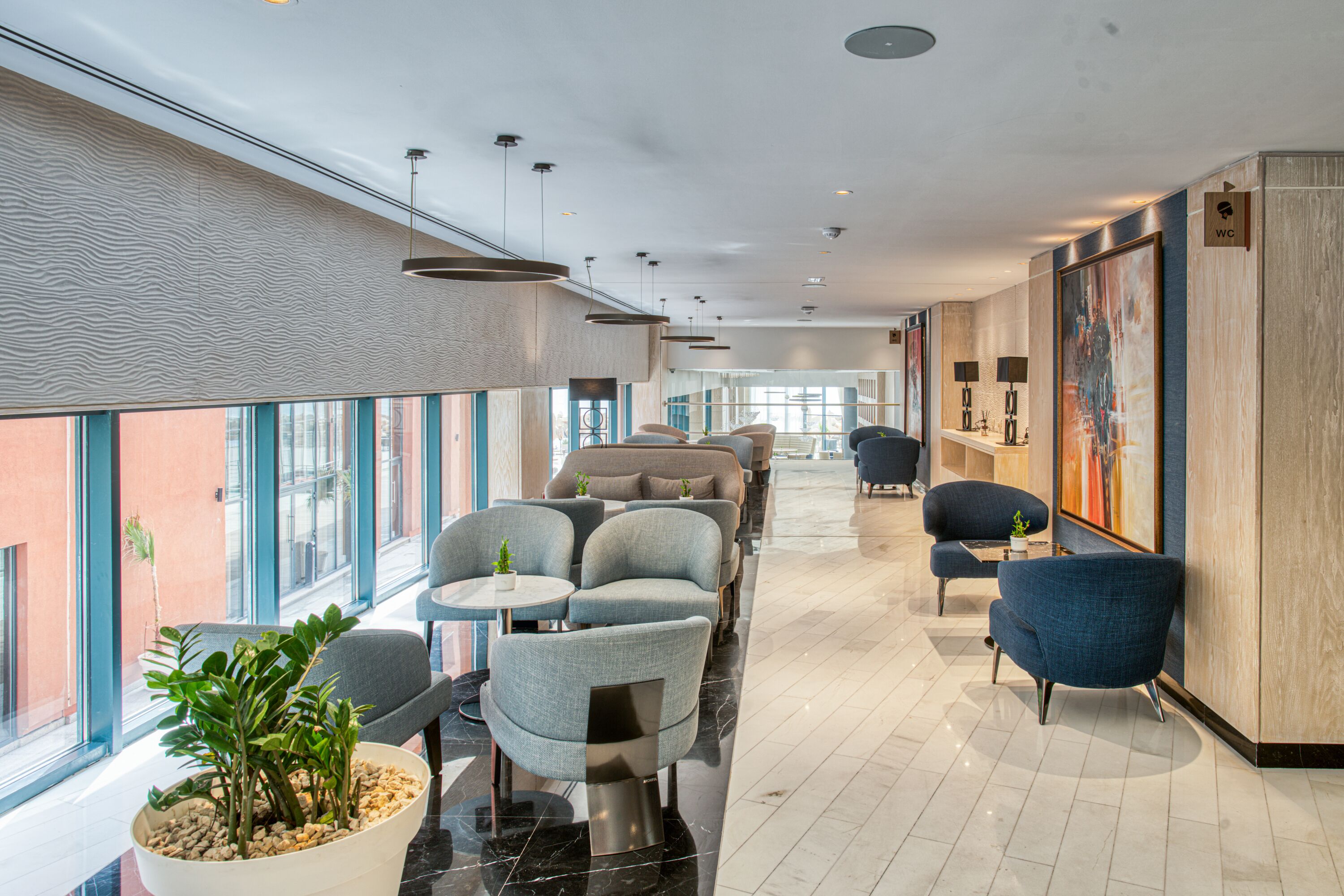 A modern hotel lobby with seating areas, large windows, and artwork on the walls.