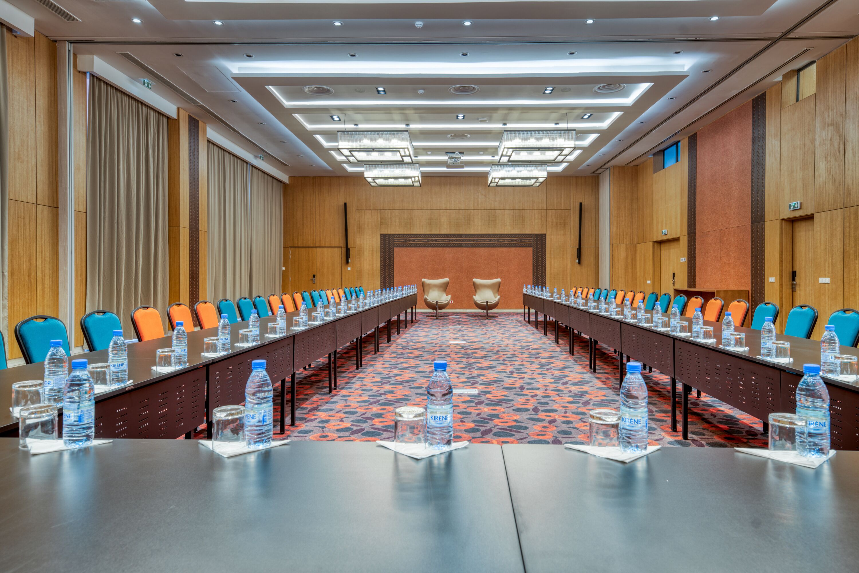 A conference room with a long table, chairs, water bottles, and a patterned carpet.
