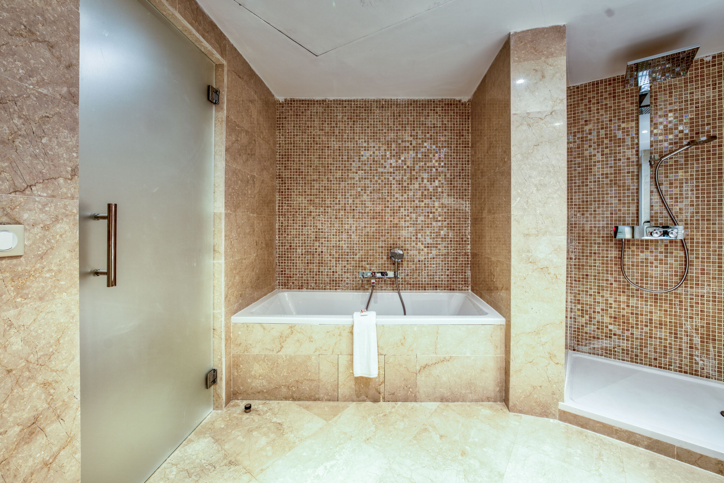 Un baño moderno con suelo de mármol, una bañera independiente y una zona de ducha con un muro de mosaico.