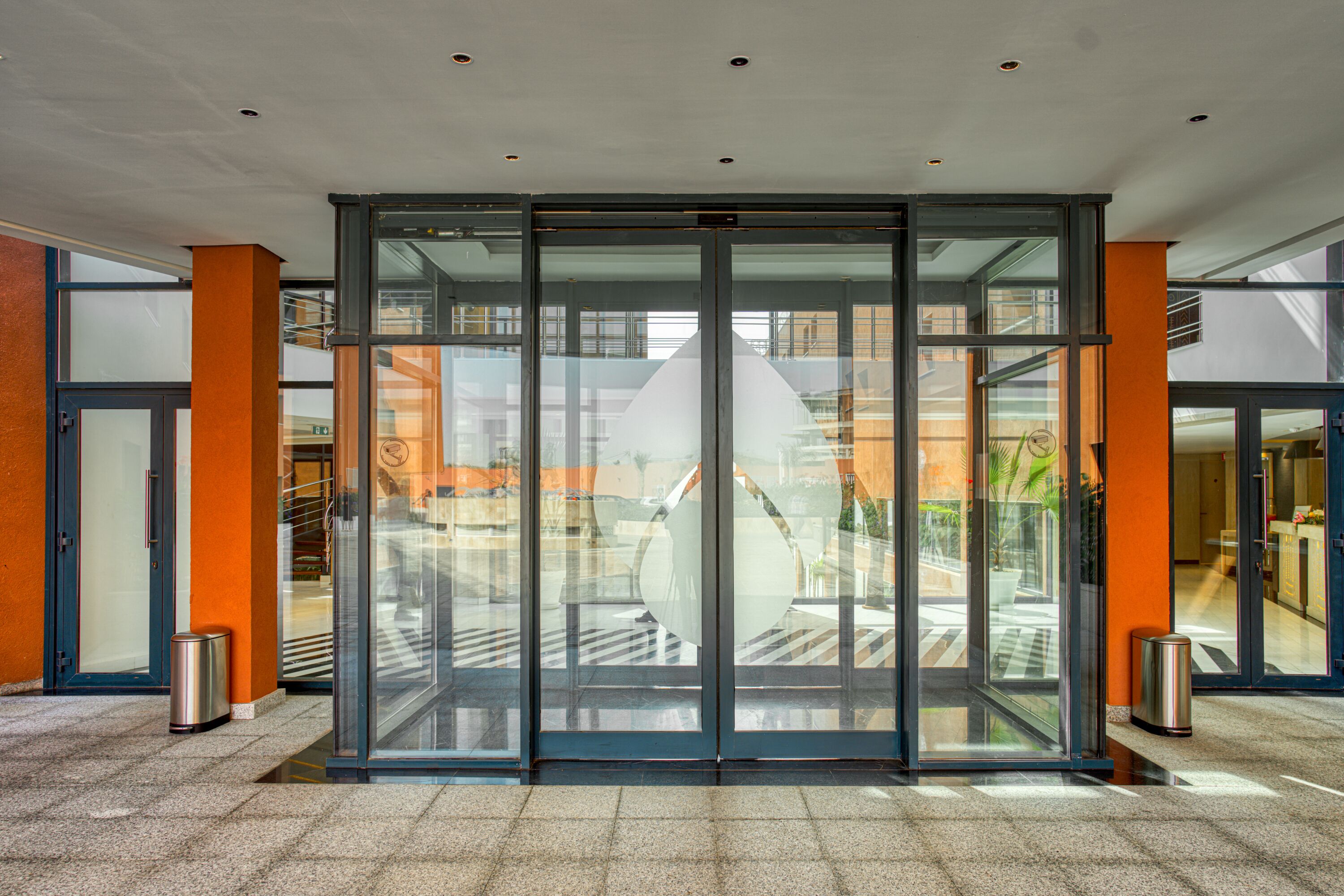 A modern hotel entrance with a revolving door, glass walls, and a tiled floor.
