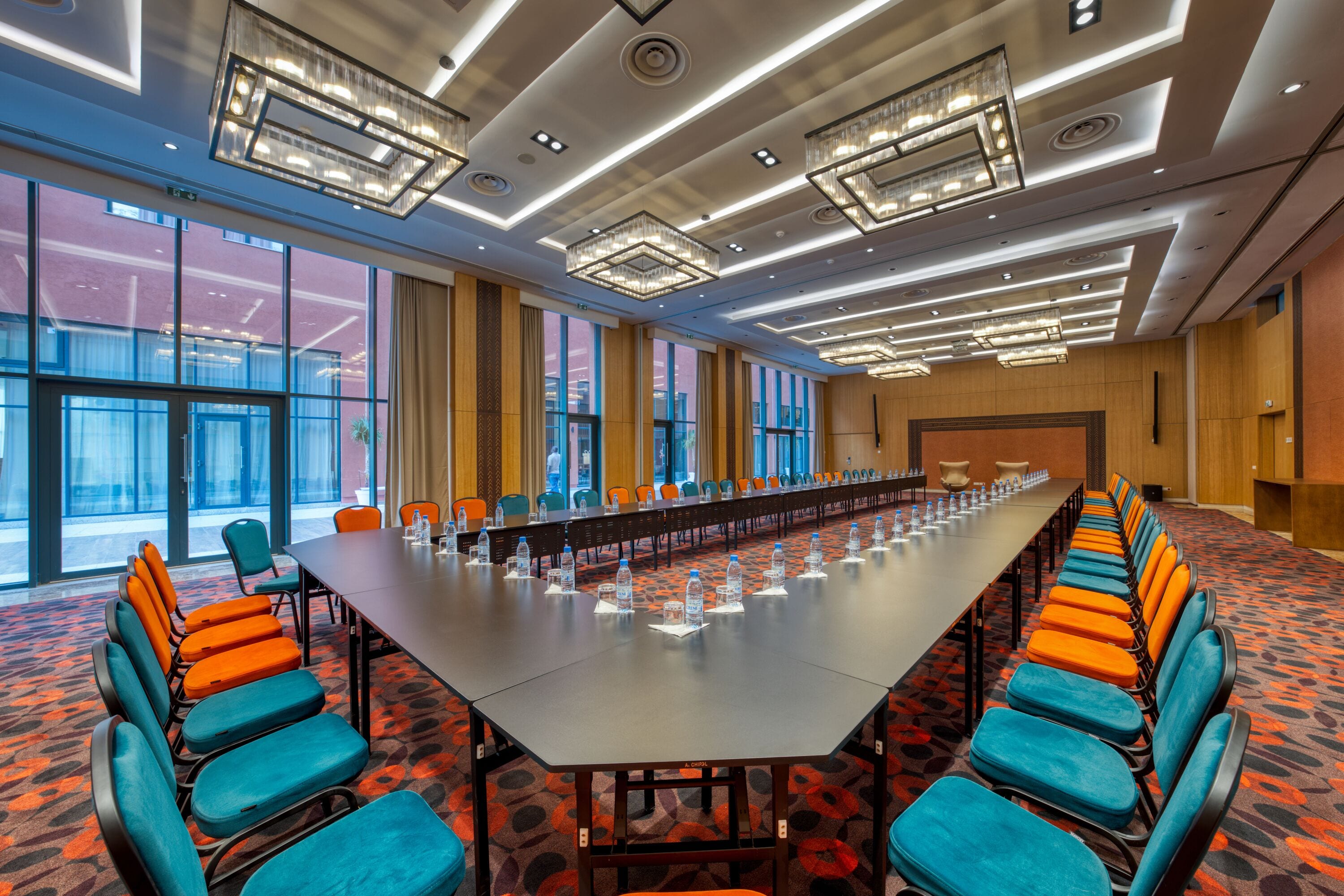 A conference room with a long table, orange and blue chairs, and a patterned carpet.