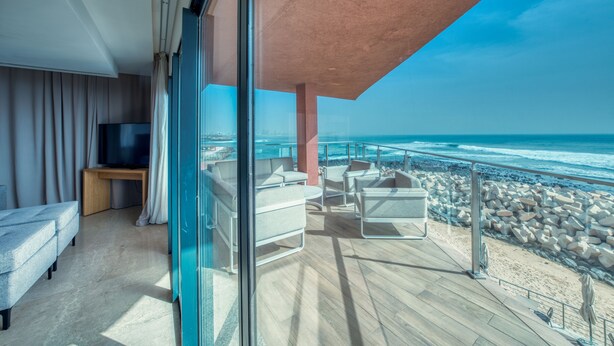 A modern balcony with a view of the ocean, furnished with white chairs and a sofa, and a television on a stand. - Azalai Hotel Dakar (Dakar)