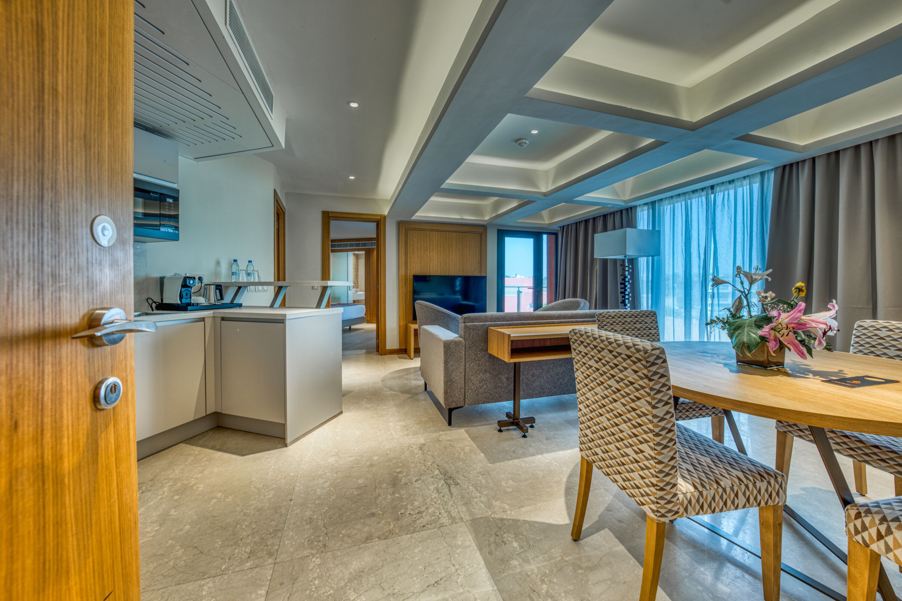 A modern hotel room with a kitchen, dining area, and a sofa.