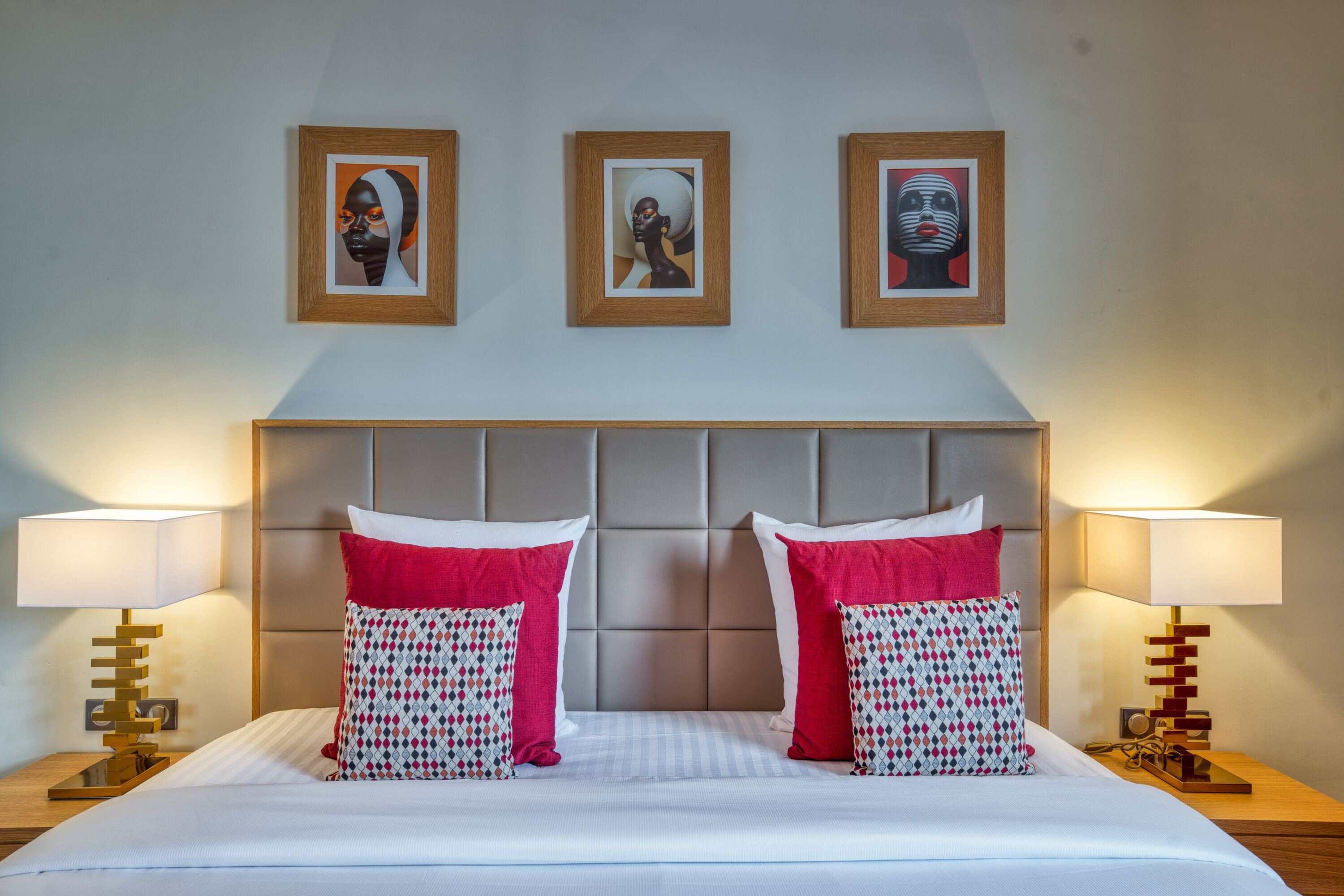 A hotel room with a large bed, two bedside tables with lamps, and three framed artworks on the wall.