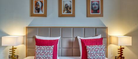 A hotel room with a large bed, two bedside tables with lamps, and three framed artworks on the wall.