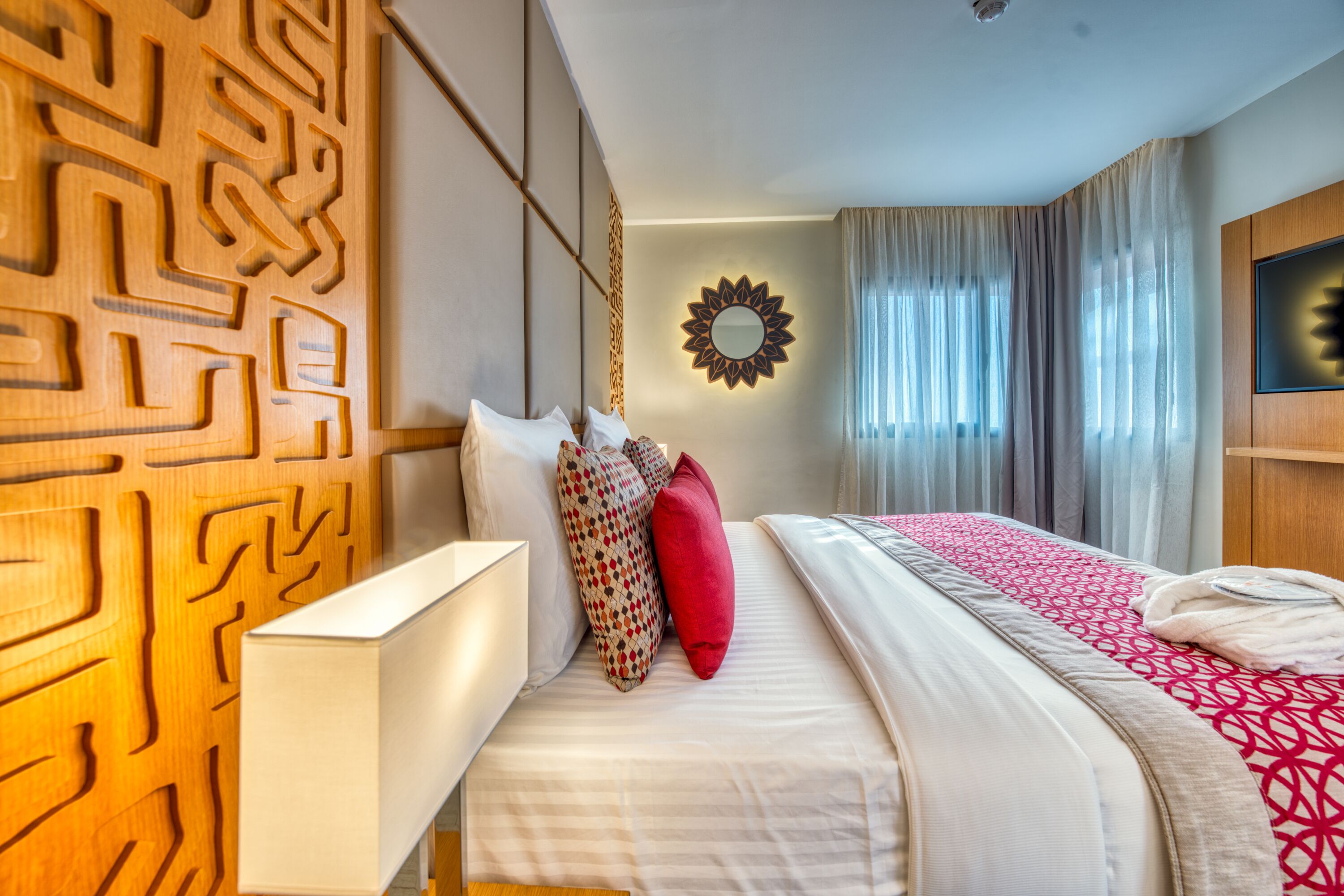 Habitación de hotel con cama, espejo en la pared y ventana con cortinas.